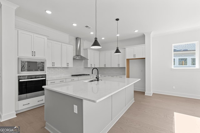 kitchen with appliances with stainless steel finishes, sink, white cabinets, wall chimney range hood, and a center island with sink