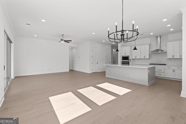 kitchen featuring built in microwave, stovetop, an island with sink, wall chimney range hood, and white cabinets