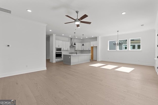 unfurnished living room featuring crown molding, sink, ceiling fan with notable chandelier, and light wood-type flooring