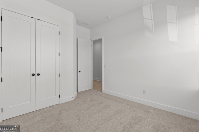 unfurnished bedroom with light colored carpet and a closet