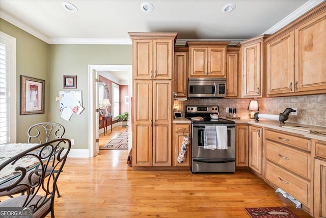 kitchen with light wood-type flooring, appliances with stainless steel finishes, a healthy amount of sunlight, and crown molding