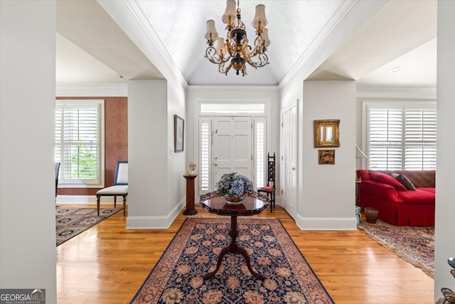 entryway with ornamental molding, lofted ceiling, a chandelier, and light hardwood / wood-style floors