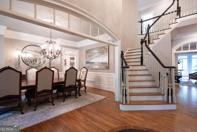 dining area featuring wood-type flooring, crown molding, a high ceiling, and an inviting chandelier