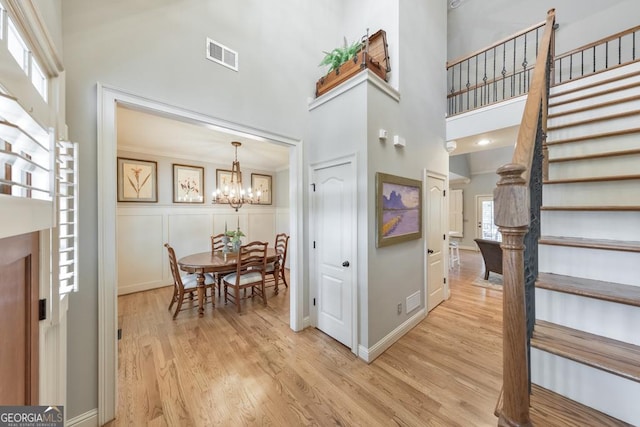 foyer entrance with a notable chandelier, light wood-type flooring, and a high ceiling