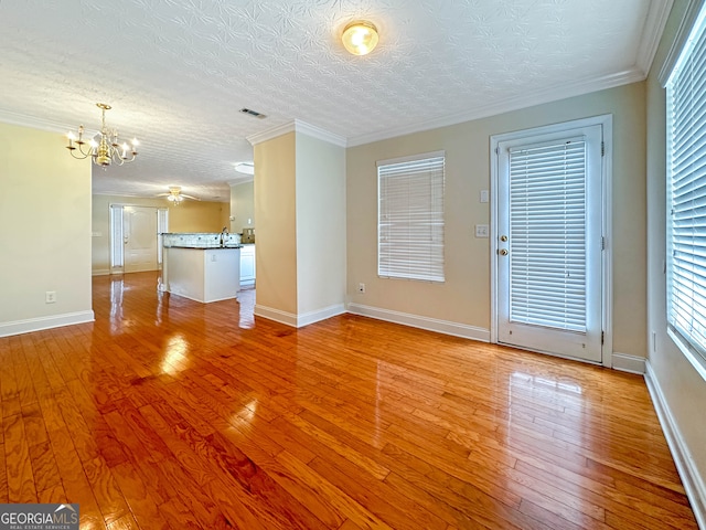 unfurnished living room featuring crown molding, an inviting chandelier, light hardwood / wood-style flooring, and a textured ceiling