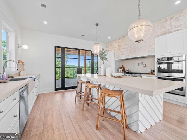 kitchen featuring light wood-type flooring, stainless steel appliances, pendant lighting, a kitchen breakfast bar, and plenty of natural light