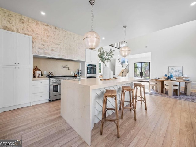 kitchen featuring white cabinets, stainless steel appliances, light hardwood / wood-style floors, pendant lighting, and a center island with sink