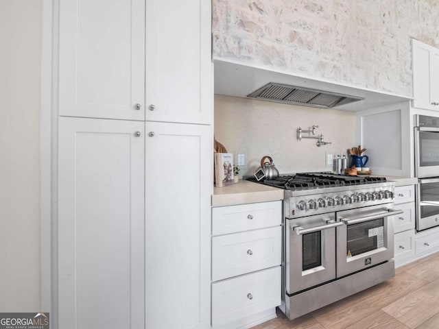 kitchen featuring white cabinetry, backsplash, light hardwood / wood-style flooring, and appliances with stainless steel finishes