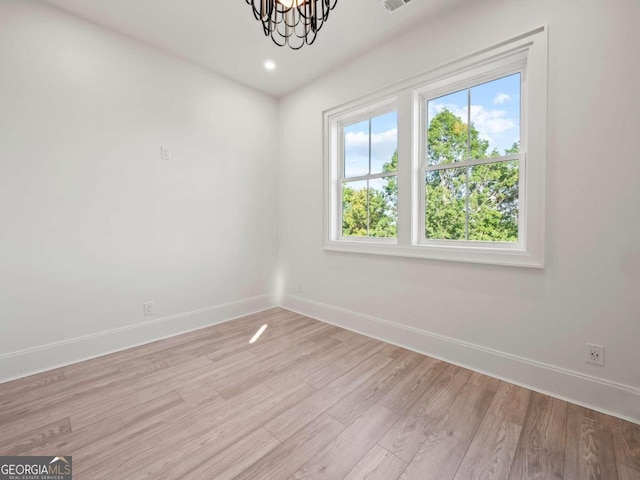 spare room featuring plenty of natural light, an inviting chandelier, and light hardwood / wood-style floors