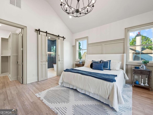 bedroom with light hardwood / wood-style floors, connected bathroom, multiple windows, and a barn door