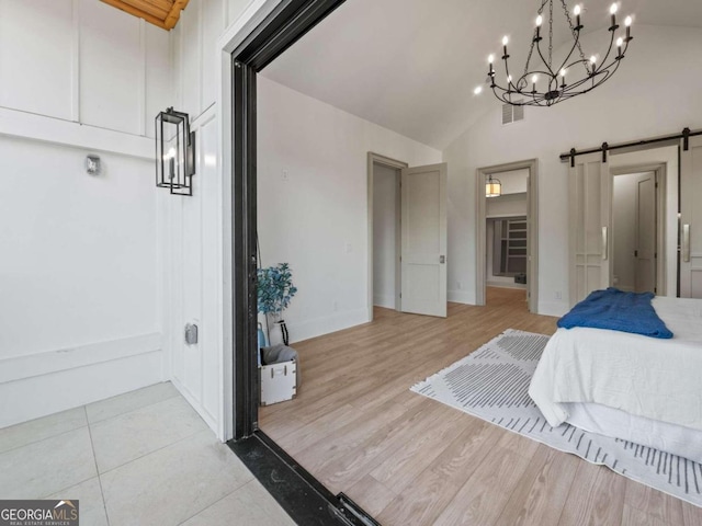 bedroom with light wood-type flooring, a barn door, and high vaulted ceiling