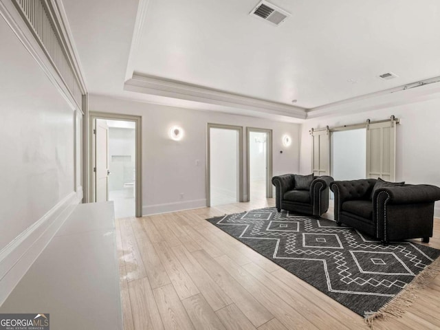 living room with hardwood / wood-style flooring, a raised ceiling, a barn door, and ornamental molding