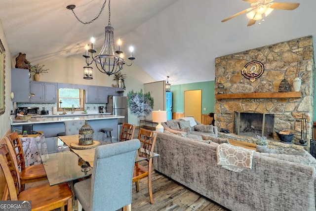 dining room with lofted ceiling, a stone fireplace, sink, wood-type flooring, and ceiling fan with notable chandelier