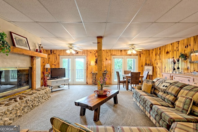 carpeted living room featuring ceiling fan, wood walls, and a drop ceiling