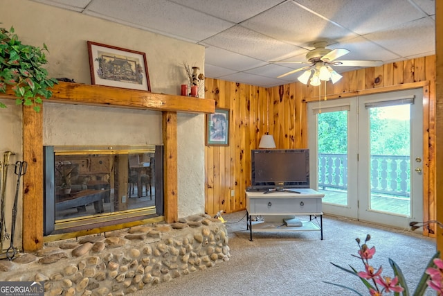 living room with a paneled ceiling, wooden walls, and carpet flooring