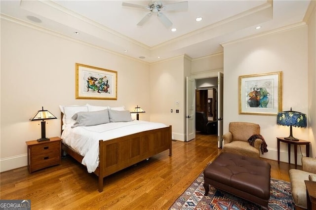 bedroom with a raised ceiling, ceiling fan, wood-type flooring, and ornamental molding