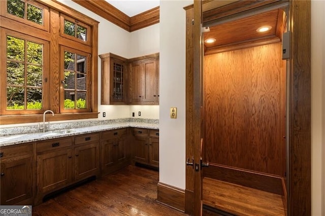 bar with sink, elevator, ornamental molding, light stone counters, and dark hardwood / wood-style flooring