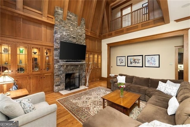 living room featuring a high ceiling, light hardwood / wood-style flooring, a stone fireplace, and wood walls