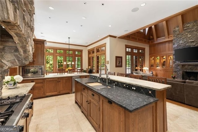 kitchen with stainless steel appliances, sink, a stone fireplace, plenty of natural light, and an island with sink