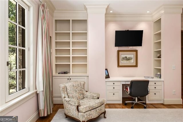 home office featuring built in shelves, ornamental molding, built in desk, and light hardwood / wood-style floors