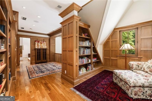 living area featuring wooden walls, built in features, crown molding, and light wood-type flooring