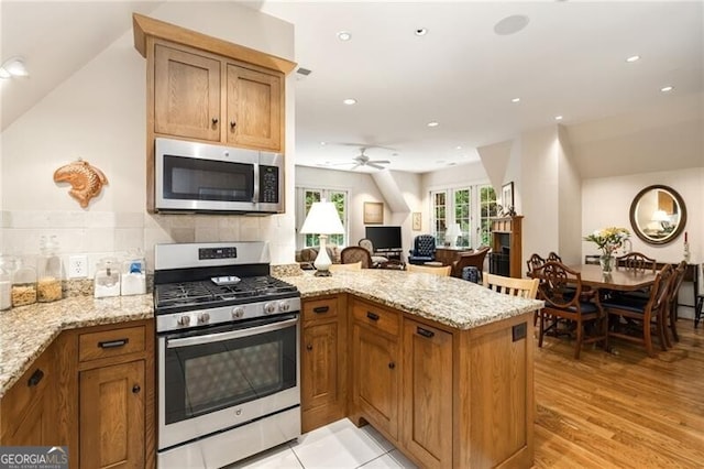 kitchen featuring ceiling fan, stainless steel appliances, light stone counters, backsplash, and kitchen peninsula