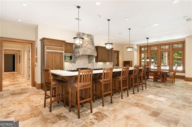 kitchen featuring stainless steel microwave, hanging light fixtures, backsplash, a spacious island, and a breakfast bar area