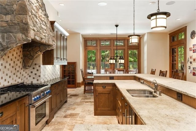 kitchen with backsplash, sink, hanging light fixtures, stainless steel stove, and light stone countertops