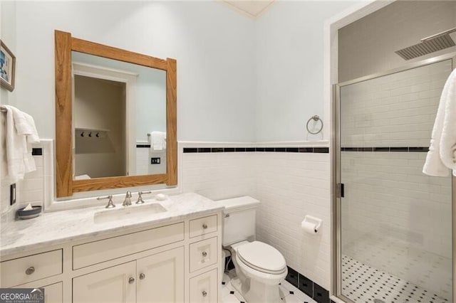 bathroom with vanity, toilet, a shower with door, and tile walls