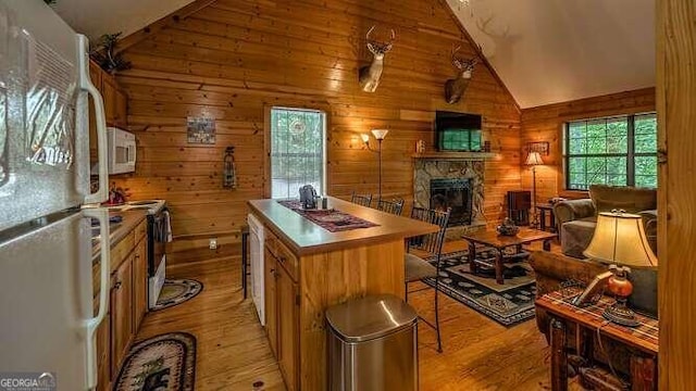 kitchen with white appliances, a kitchen island, a stone fireplace, light hardwood / wood-style floors, and vaulted ceiling