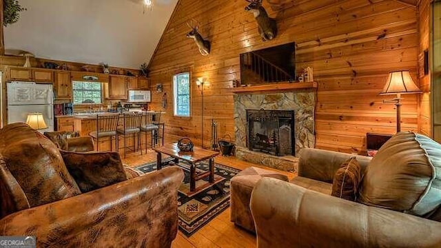 living room with light hardwood / wood-style flooring, high vaulted ceiling, a fireplace, and wooden walls