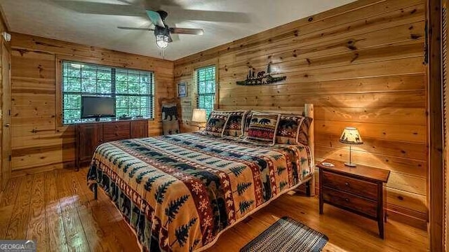 bedroom with ceiling fan, wood walls, and wood-type flooring