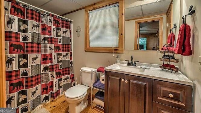 bathroom featuring hardwood / wood-style floors, toilet, vanity, a drop ceiling, and curtained shower