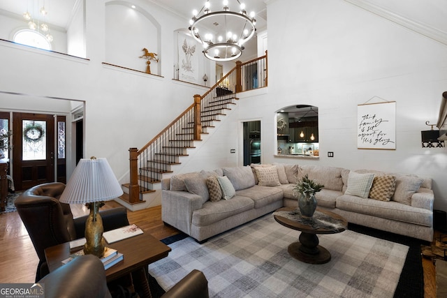 living room with an inviting chandelier, hardwood / wood-style flooring, crown molding, and a high ceiling