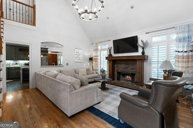 living room featuring dark hardwood / wood-style flooring, a stone fireplace, high vaulted ceiling, and an inviting chandelier