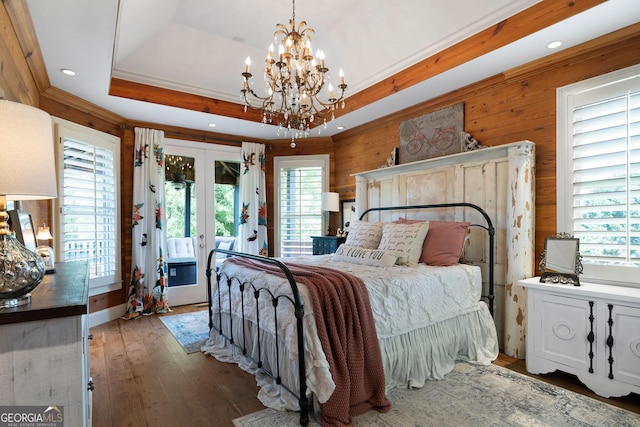 bedroom featuring access to exterior, a raised ceiling, hardwood / wood-style floors, and multiple windows