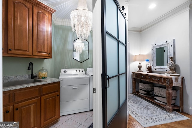 laundry area featuring light tile patterned flooring, sink, ornamental molding, a notable chandelier, and washing machine and dryer