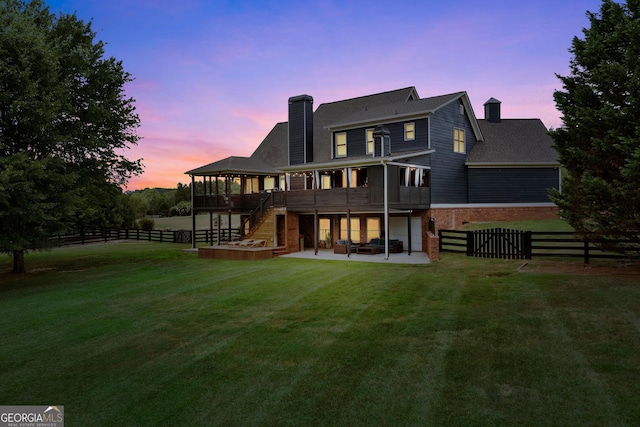 back house at dusk with a patio, a wooden deck, and a lawn