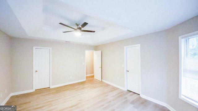 unfurnished bedroom featuring a raised ceiling, ceiling fan, and light hardwood / wood-style floors