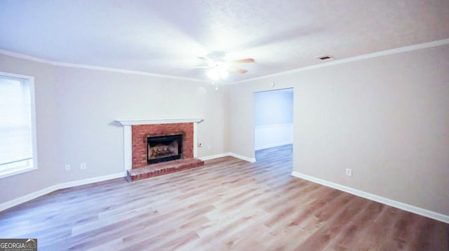 unfurnished living room featuring a brick fireplace, light wood-type flooring, ceiling fan, and crown molding