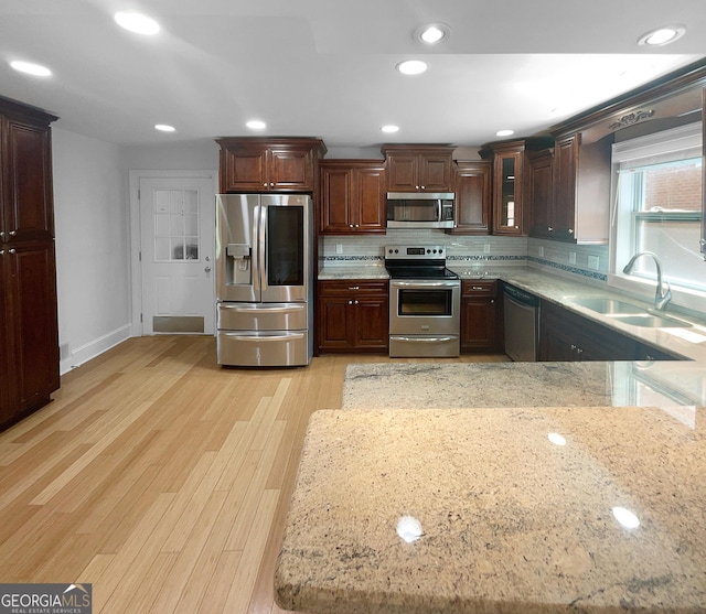 kitchen with light stone countertops, appliances with stainless steel finishes, backsplash, and light wood-type flooring