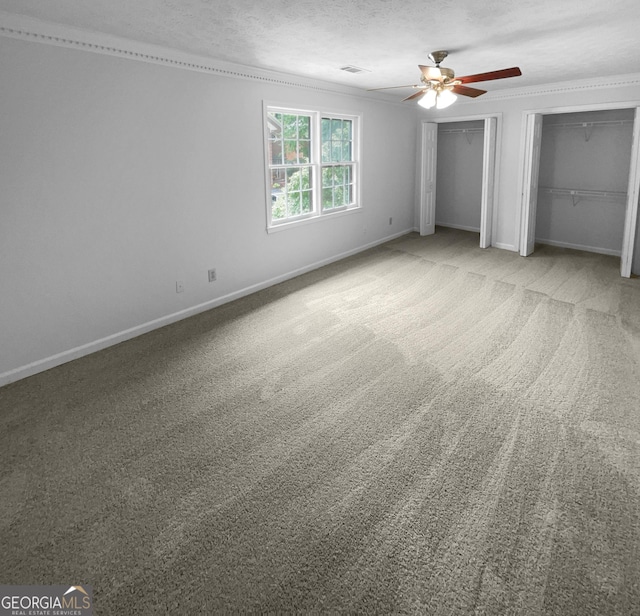 unfurnished bedroom featuring multiple closets, ceiling fan, light carpet, and a textured ceiling