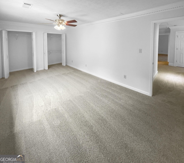 unfurnished bedroom with carpet flooring, ceiling fan, crown molding, and two closets