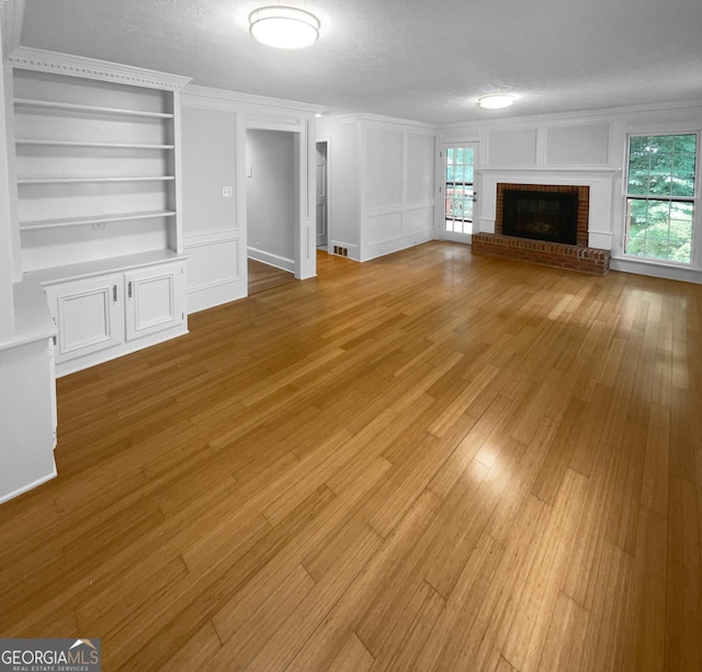 unfurnished living room with a fireplace, a textured ceiling, light hardwood / wood-style flooring, and built in features