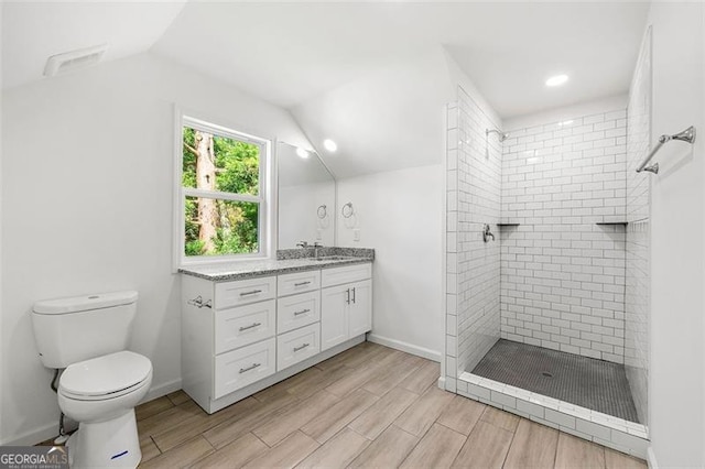 bathroom with lofted ceiling, toilet, vanity, and a tile shower