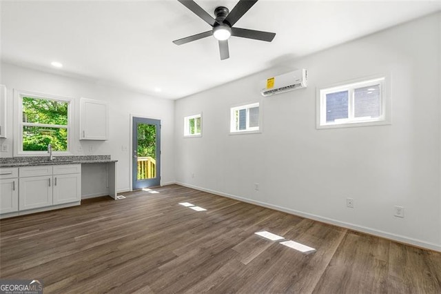 unfurnished living room with dark hardwood / wood-style flooring, sink, an AC wall unit, and ceiling fan