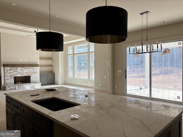 kitchen featuring hanging light fixtures, light stone countertops, sink, and a stone fireplace