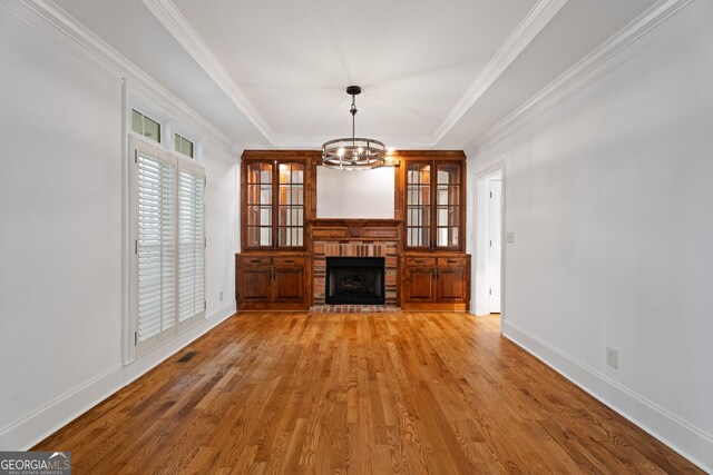 unfurnished living room with a fireplace, a raised ceiling, a chandelier, wood-type flooring, and ornamental molding