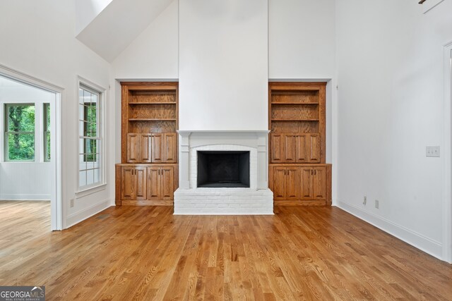 unfurnished living room featuring high vaulted ceiling, a fireplace, and light hardwood / wood-style floors