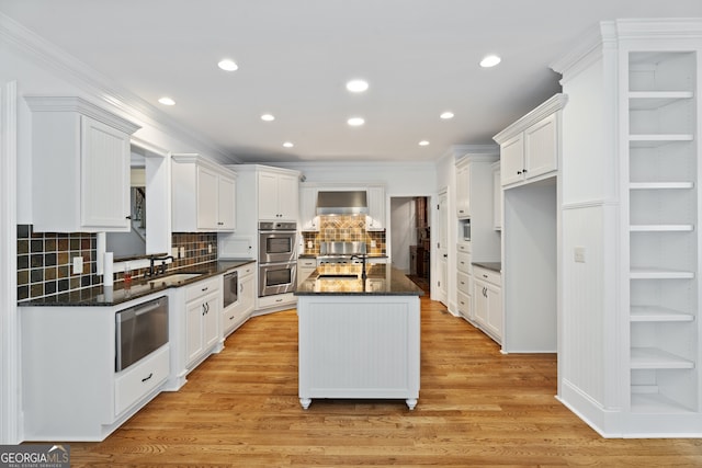 kitchen with white cabinetry, an island with sink, and wall chimney range hood